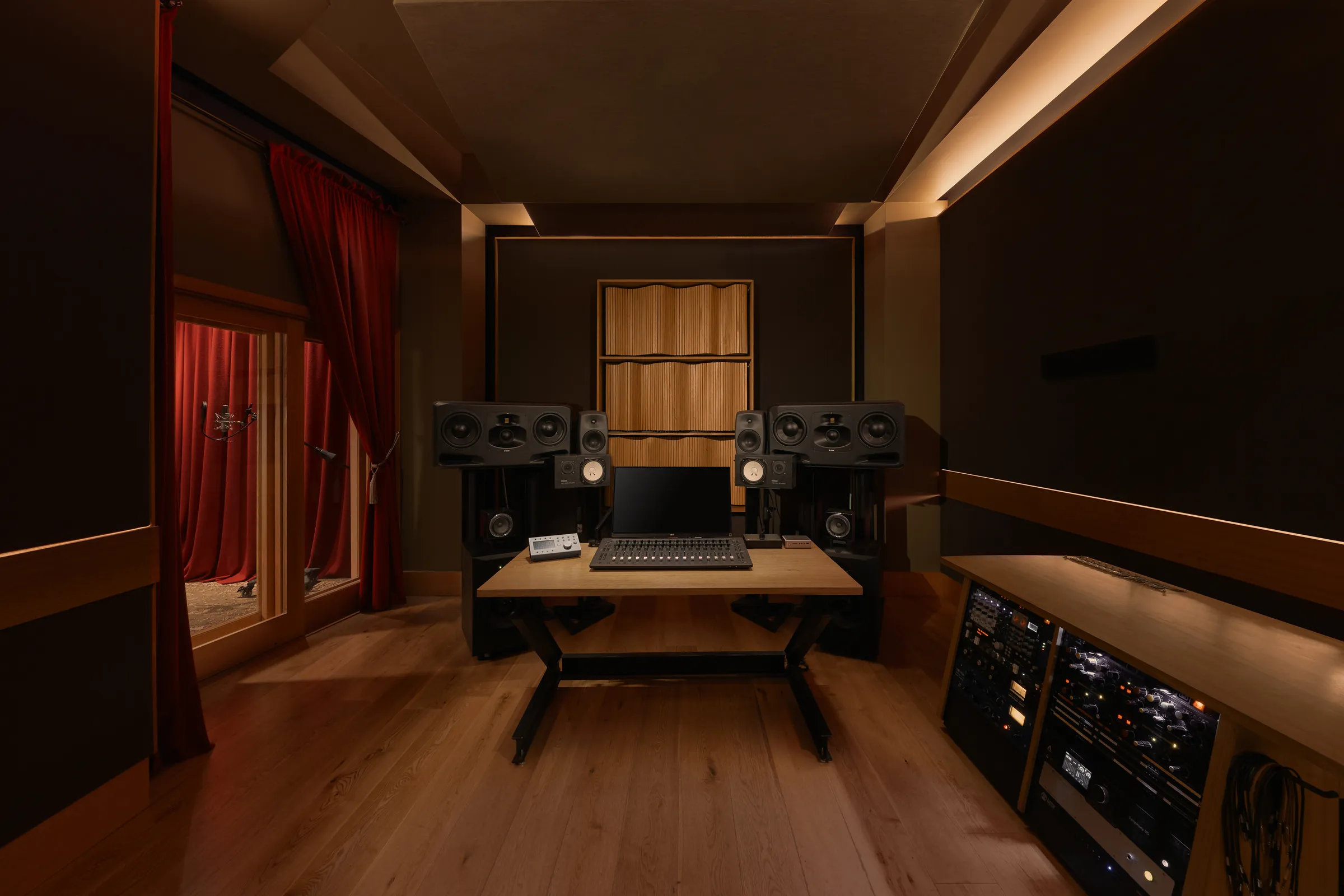The Kiln Studios control room - main monitors flanking the desk, timber acoustic panelling and red curtains under warm light